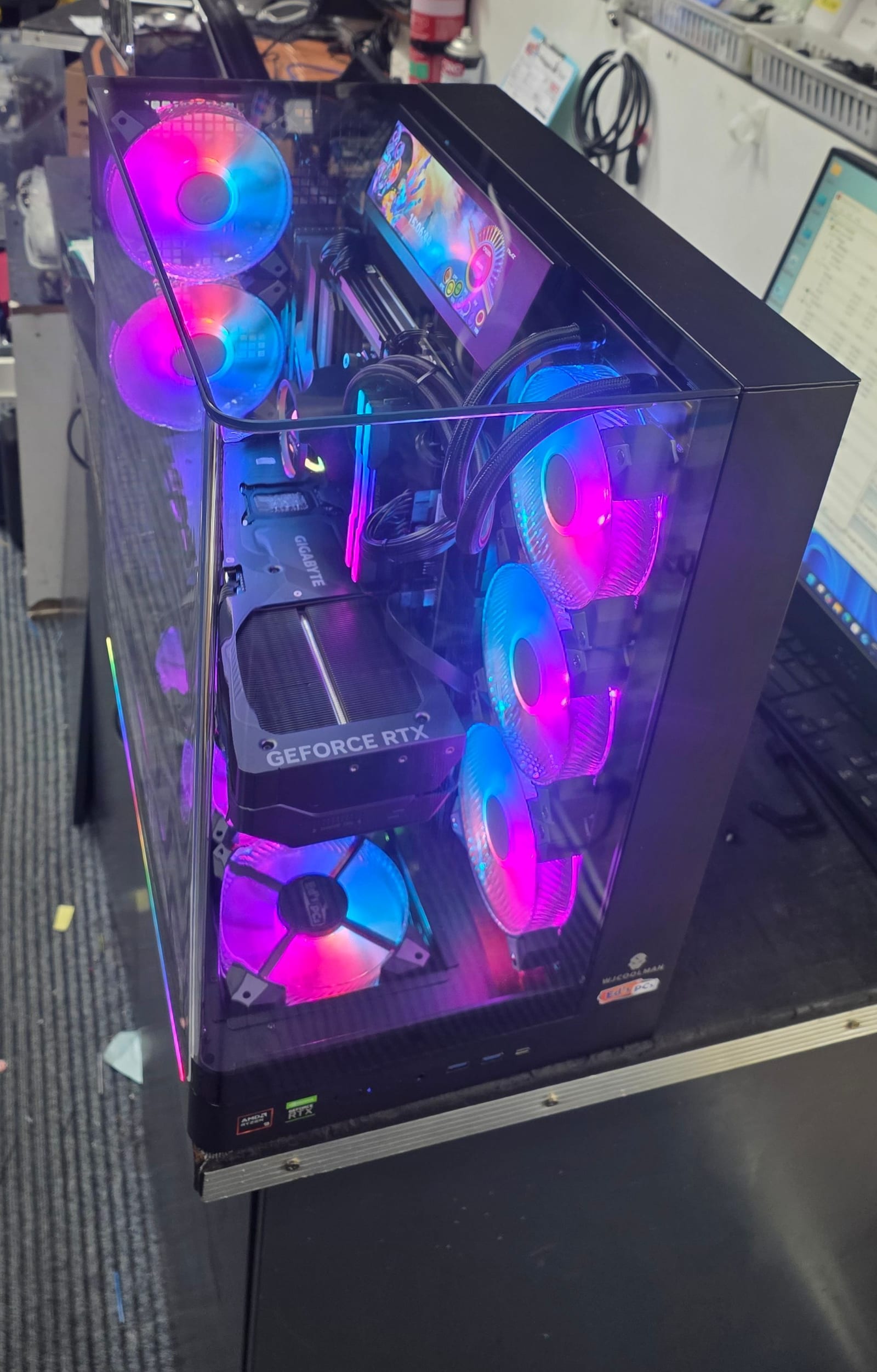 The build on the bench with a monitor beside it showing a live hardware benchmark mid-run