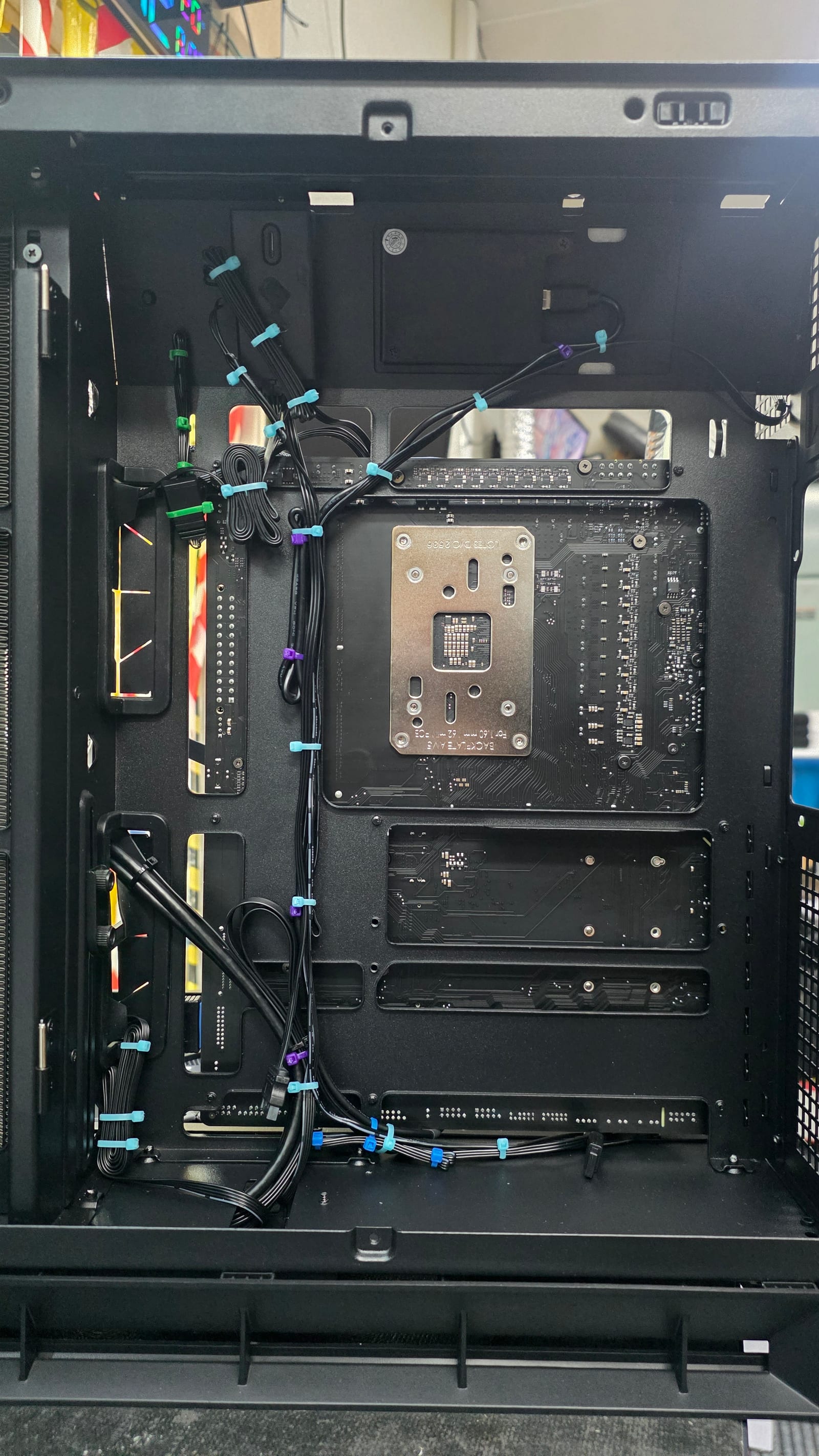 Behind the motherboard tray of a black PC case, showing power and fan cables routed and zip-tied by colour