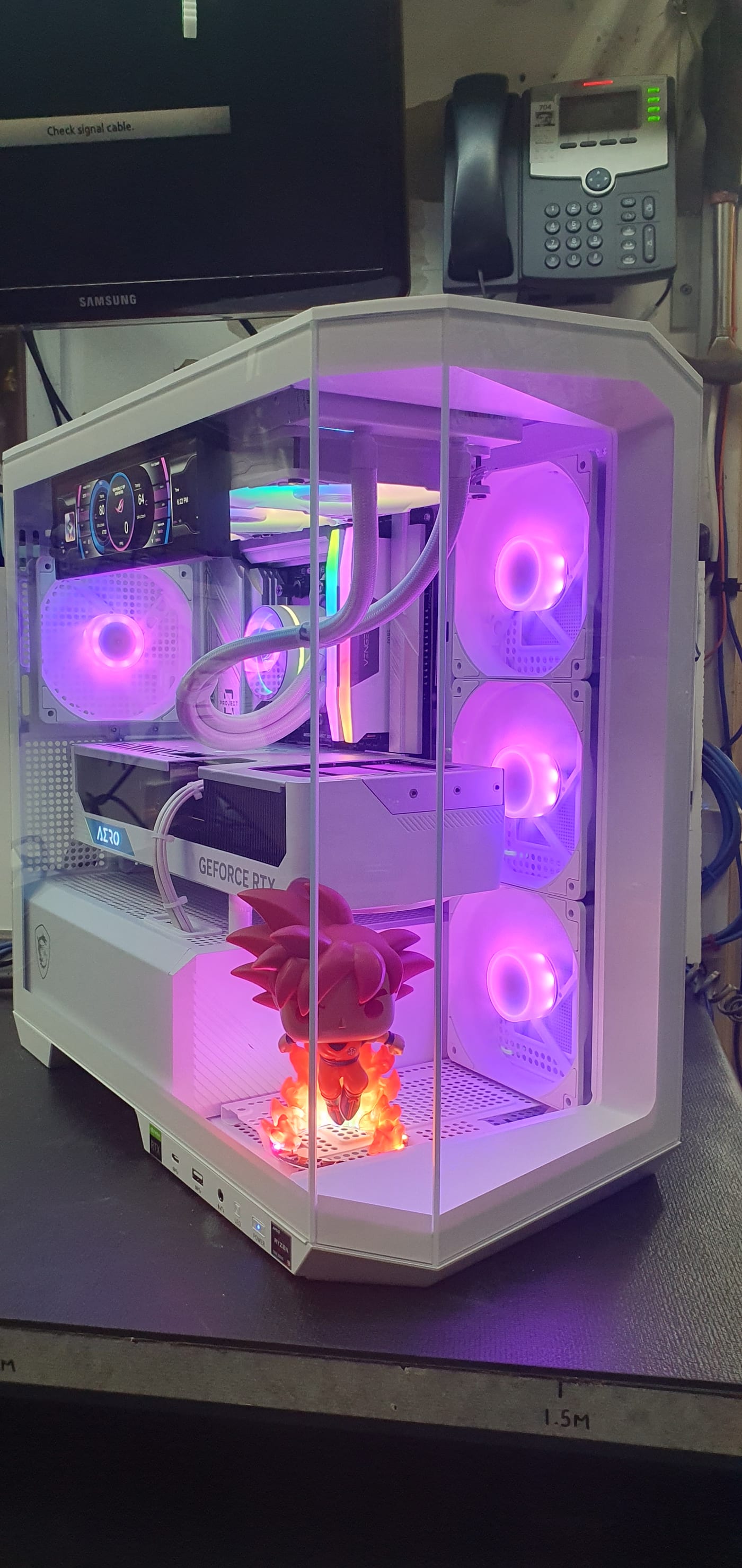 A white showcase PC tower lit purple, with three side-mounted RGB fans, a small display panel showing temperatures, and a lit figure standing in the lower chamber