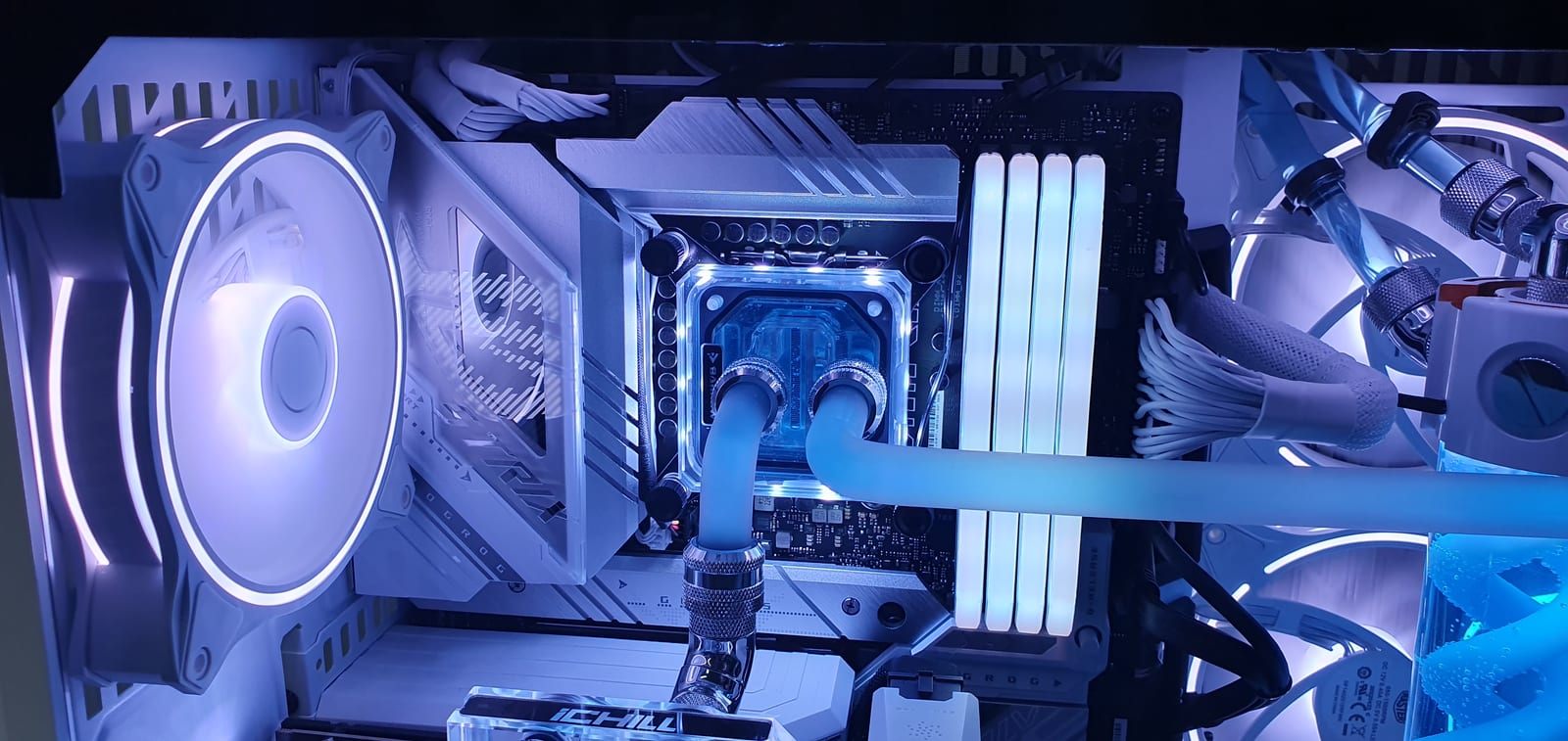 Close view of a clear CPU water block with chrome compression fittings, lit white and blue, with white RGB memory alongside