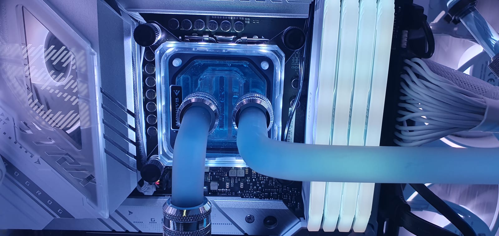 Close view of the clear CPU water block with chrome compression fittings and lit blue coolant