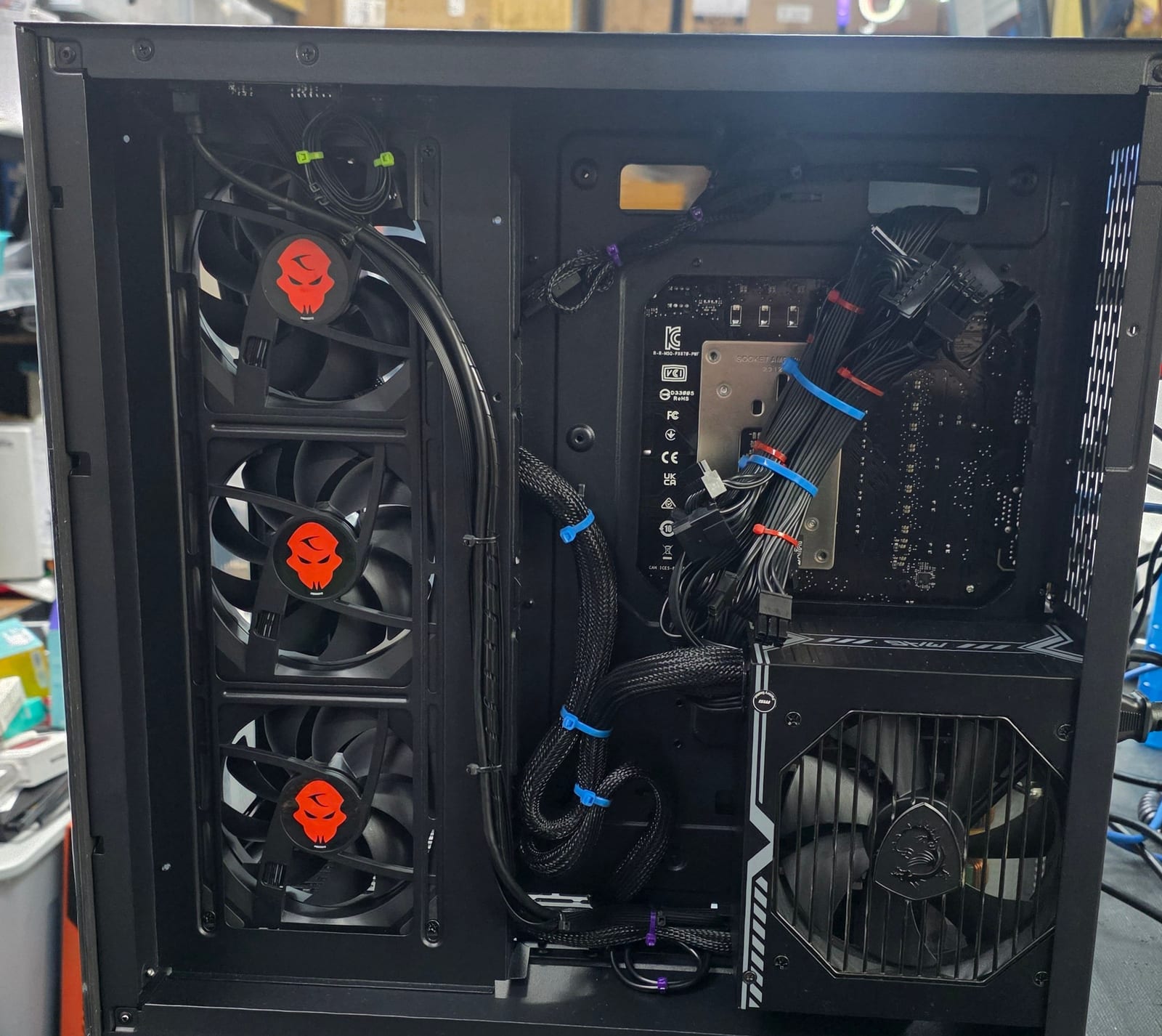 Behind the motherboard tray of the black case, cables routed and zip-tied by colour