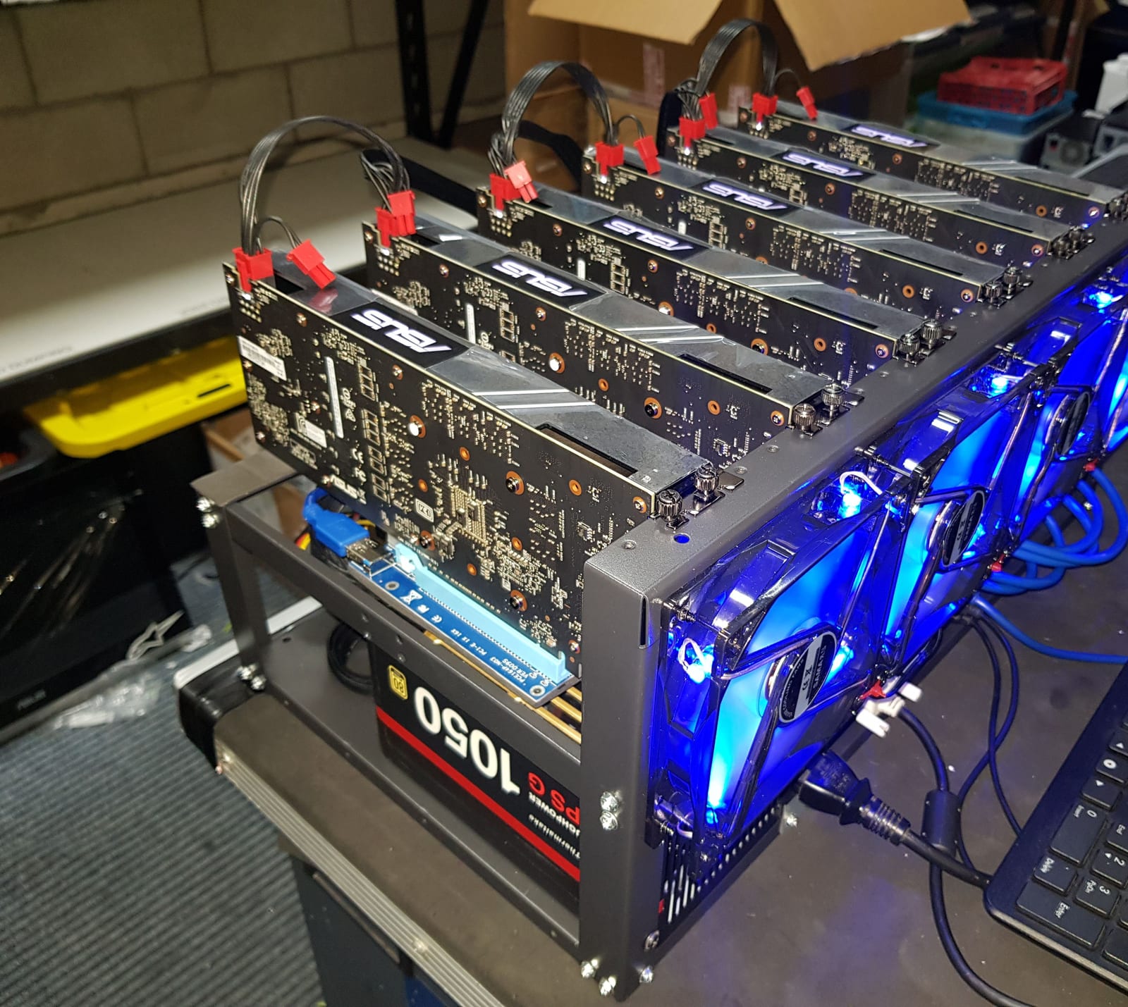 The finished open-frame mining rig from the side, graphics cards in a row above the power supply, blue LED fans lit at the front