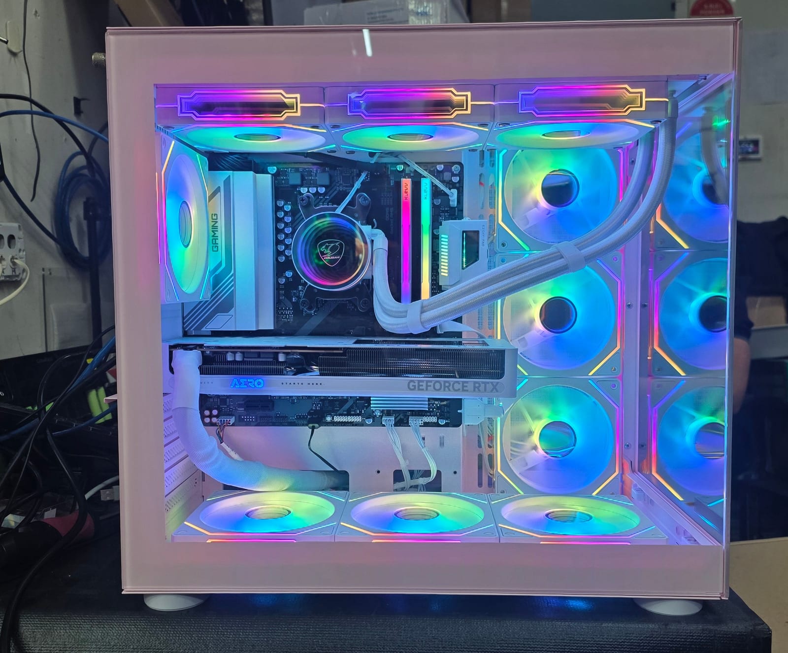 A pink PC case with nine RGB fans lit in a rainbow profile, showing a GIGABYTE AERO GeForce RTX graphics card and white-sleeved cables