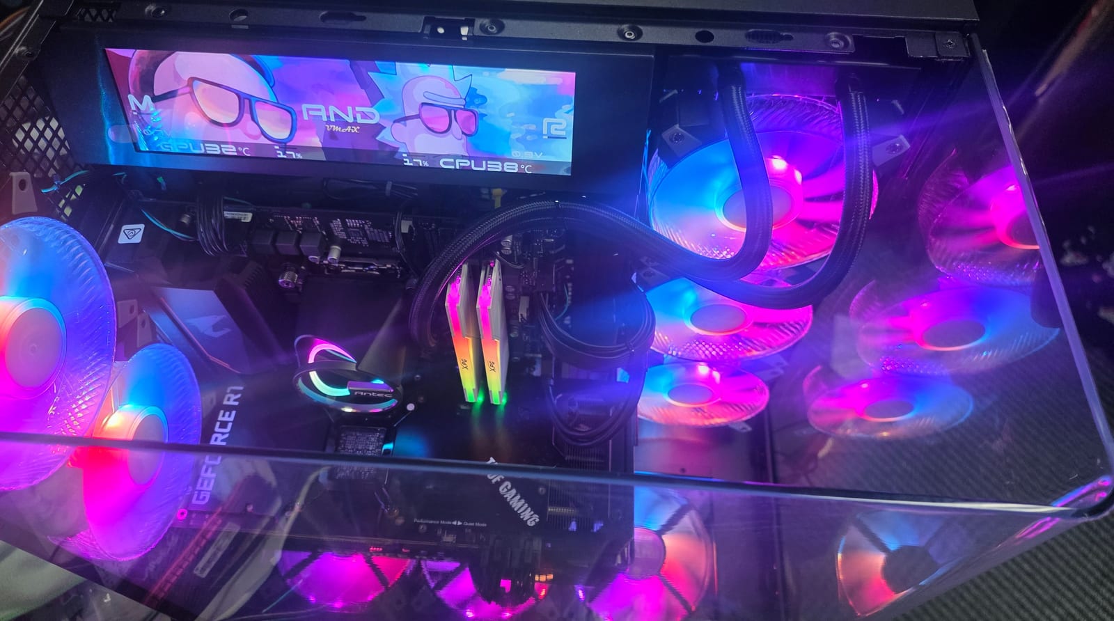 Looking down into the same case: the in-case screen showing CPU temperatures over Rick and Morty artwork, above the RGB fans and memory
