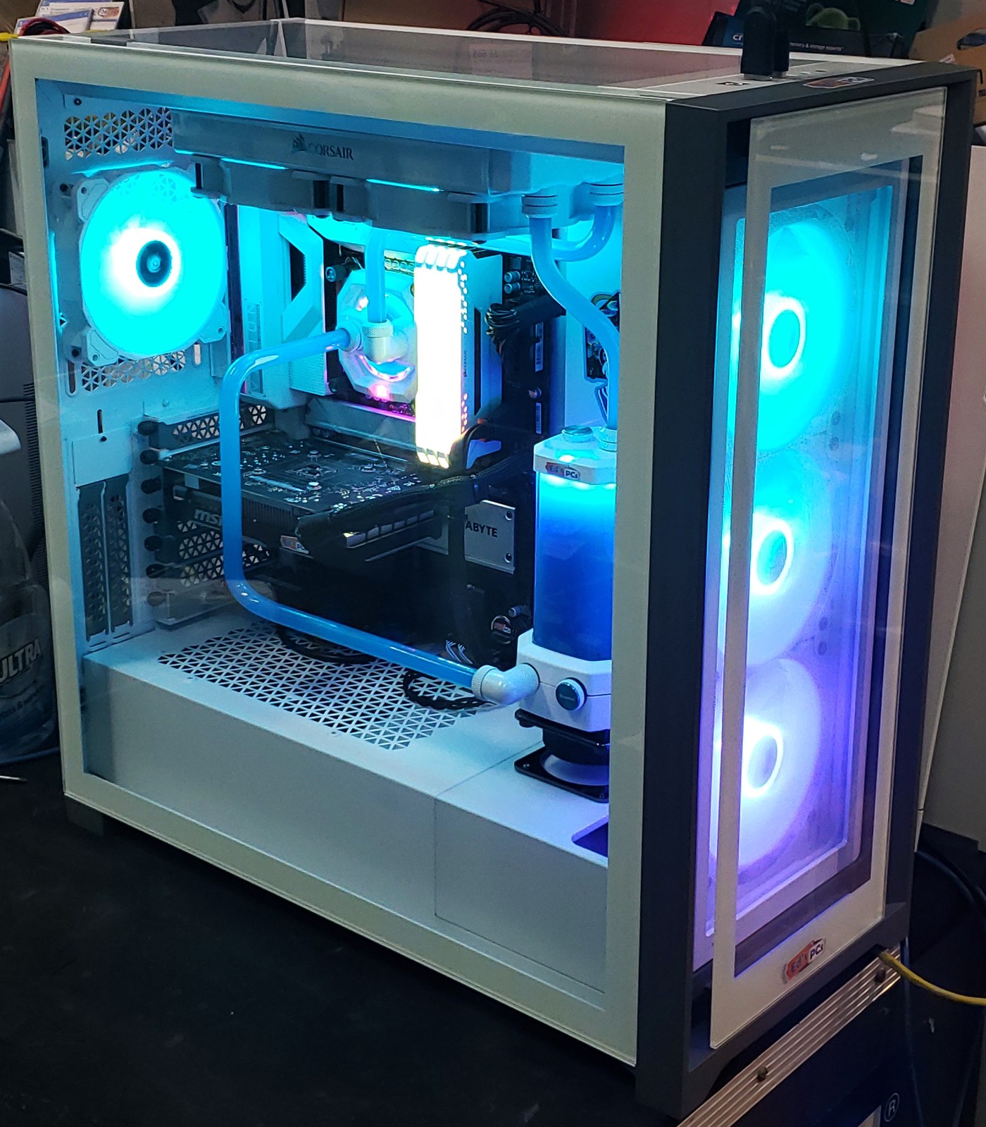 The complete white Corsair tower on the workshop bench, lit teal, with three RGB front fans and an Ed’s PCs badge on the front panel