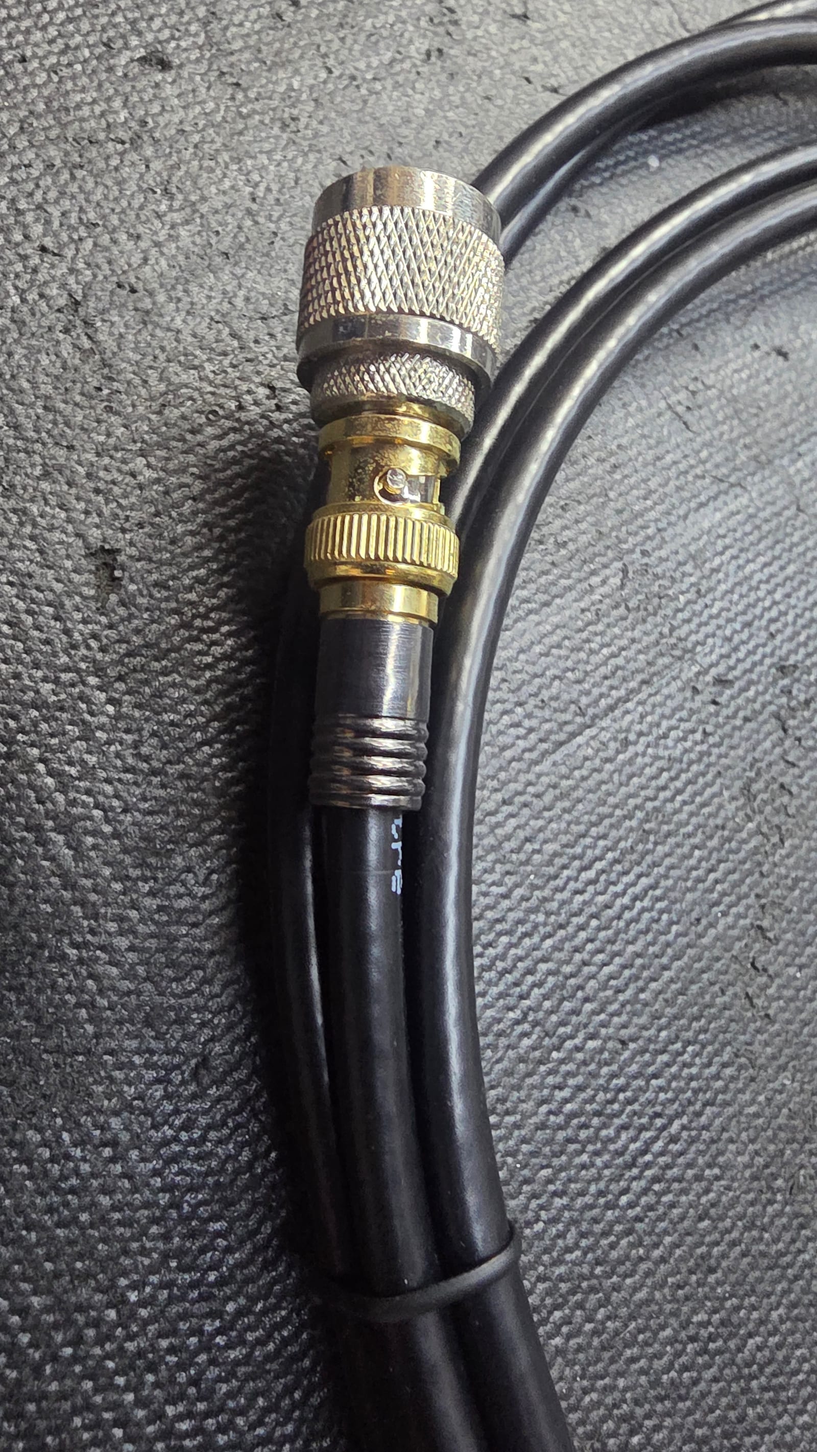 A custom-made coaxial cable with a gold BNC connector and an N-type adapter, coiled on the bench mat