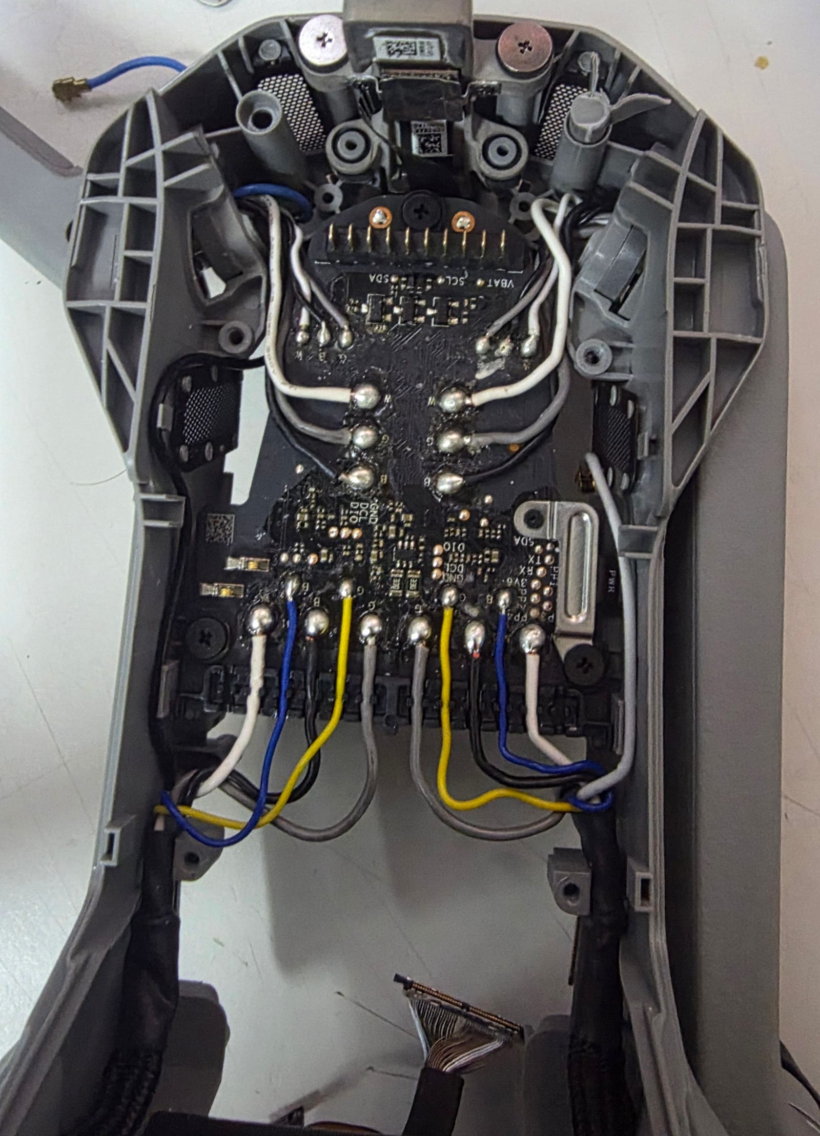 The inside of a drone on the workbench, shell opened to show the flight board with motor wiring hand-soldered to it