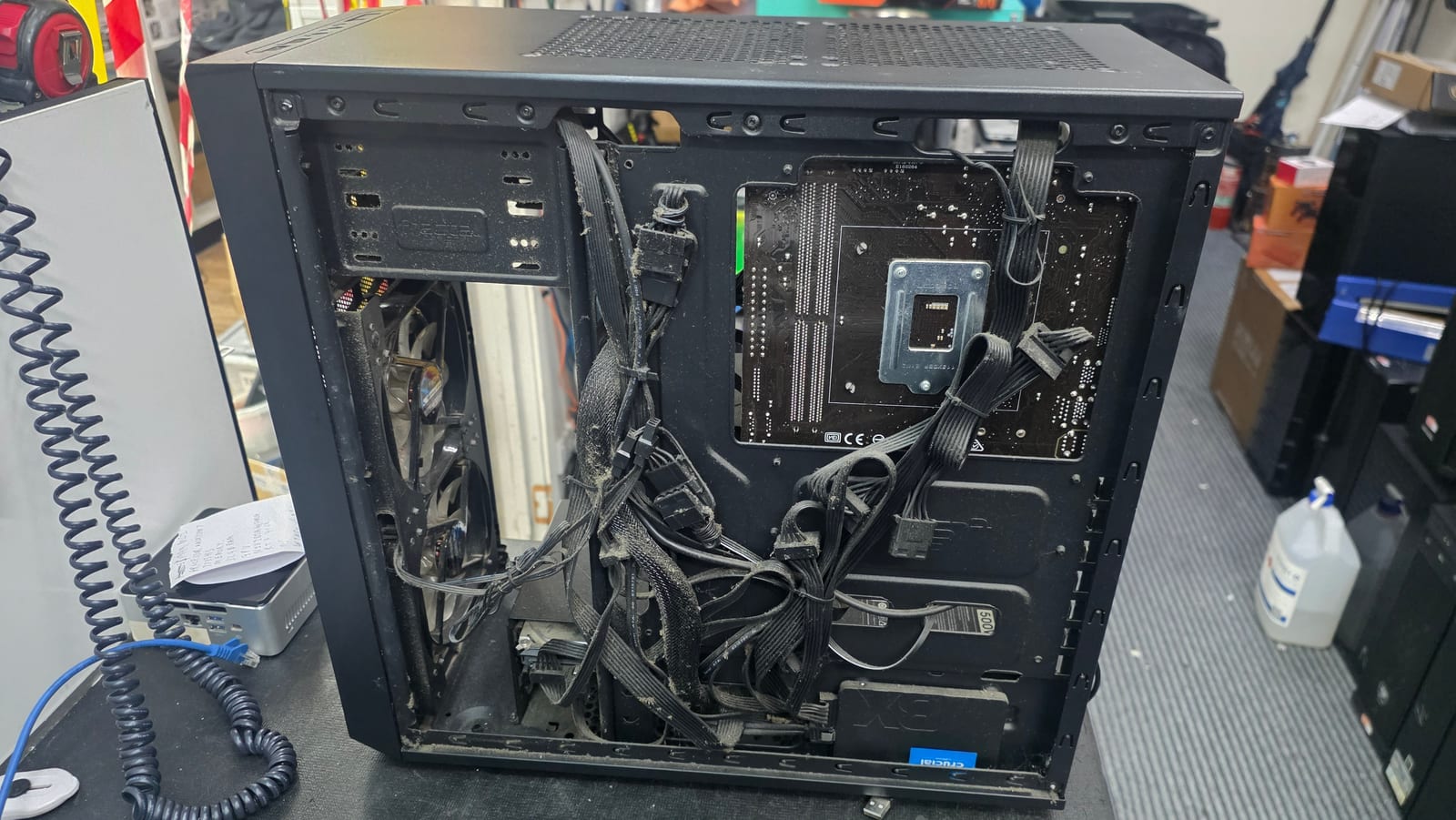 The inside of a PC case with dozens of dusty, tangled cables crammed in with no routing or colour grouping