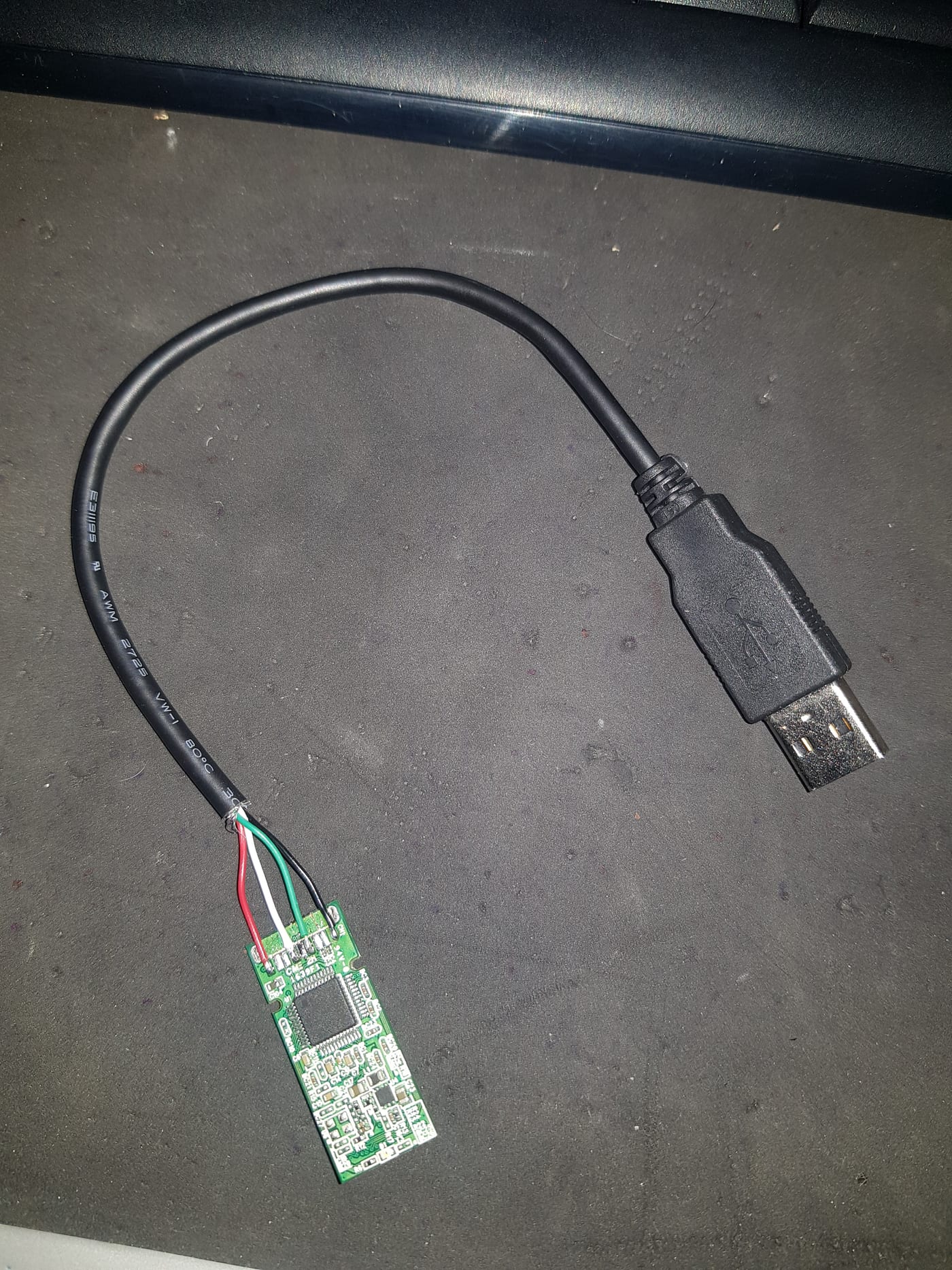 A bare USB drive circuit board with the four wires of a donor cable soldered individually onto its contact pads
